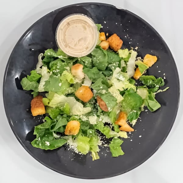 Caesar salad with croutons, parmesan cheese, and dressing on a dark plate.