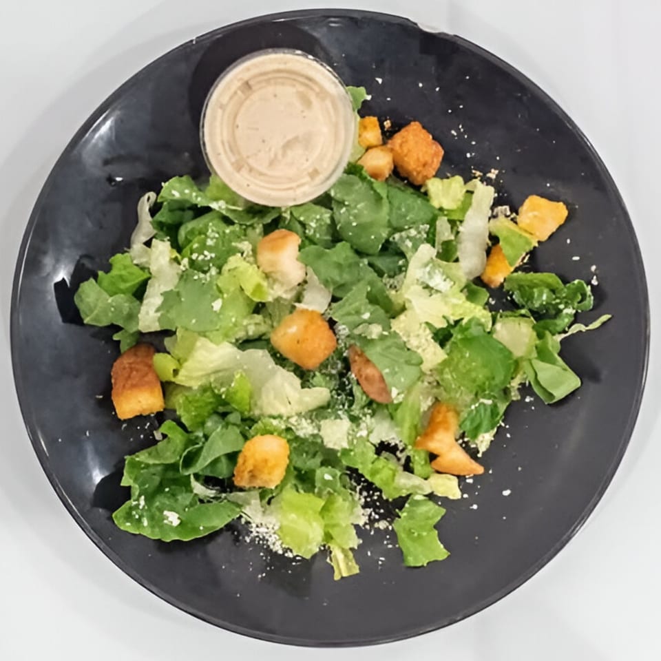 Caesar salad with croutons, parmesan cheese, and dressing on a dark plate.