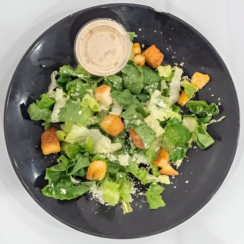 Caesar salad with croutons, parmesan cheese, and dressing on a dark plate.