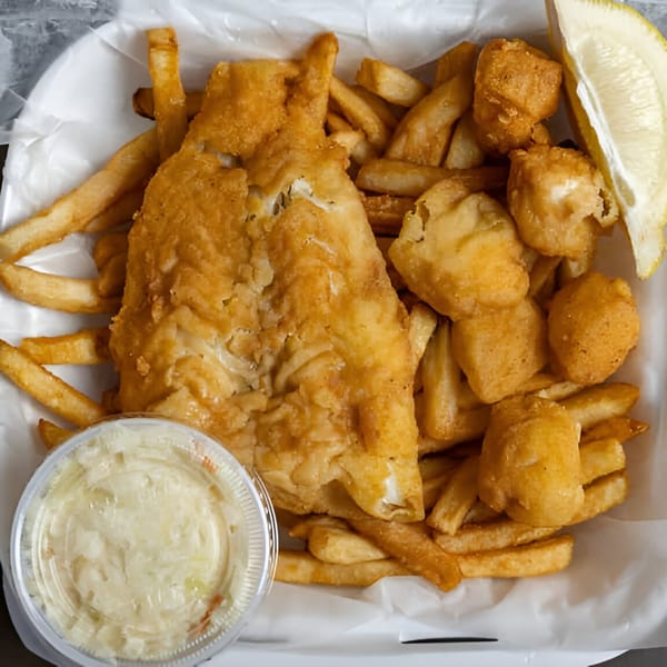 Golden-brown fried fish, fries, clam strips, tartar sauce, and a lemon wedge in a white container.