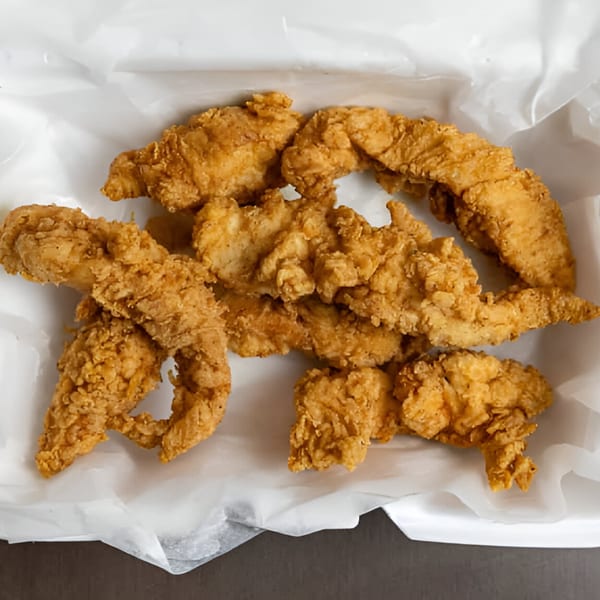 Golden-brown, crispy fried chicken tenders in a white paper-lined container, ready to eat.